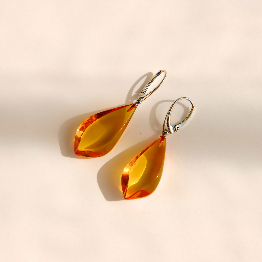 Teardrop-shaped Baltic amber drop earrings with silver leverback hooks, displayed on a warm beige background with soft shadows.