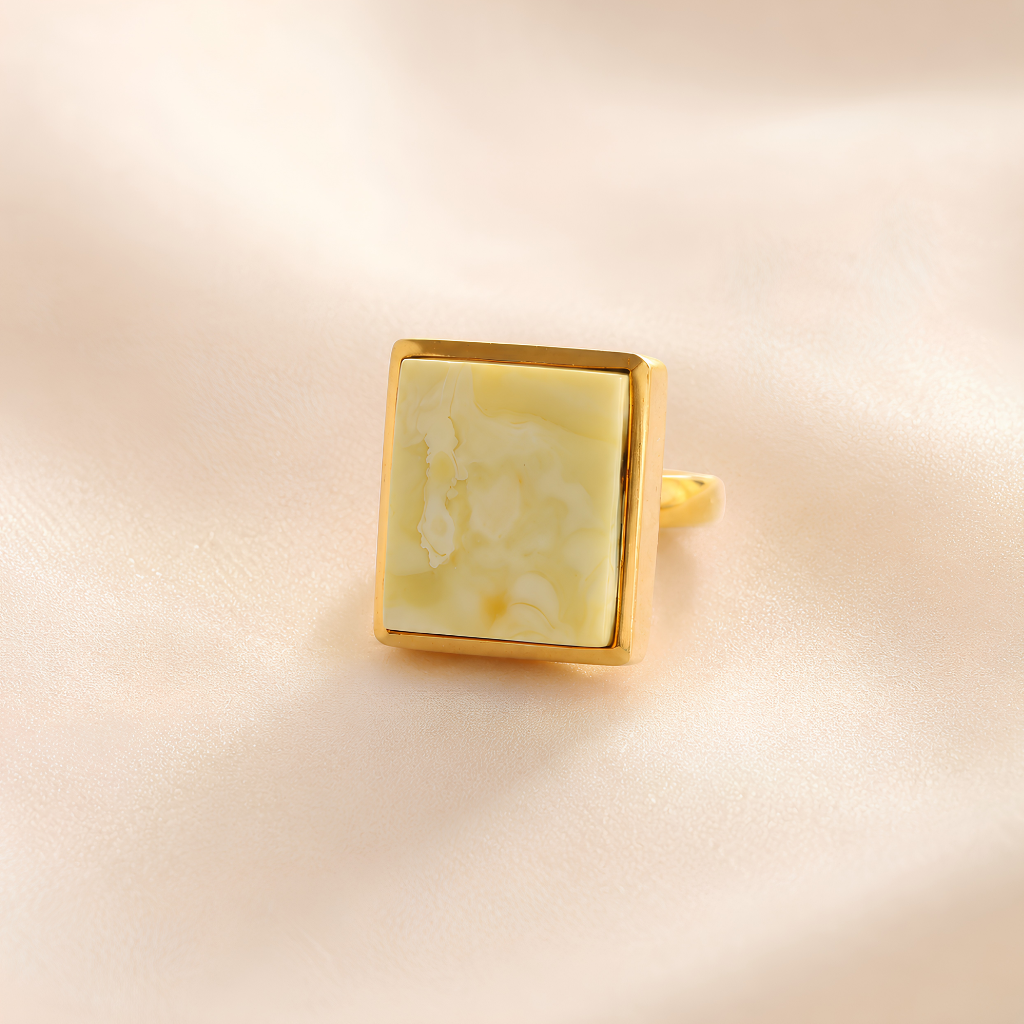 Gold amber ring with a square, light-colored stone on a beige background