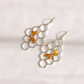 A pair of silver-toned dangle bee earrings featuring a honeycomb pattern with small amber-orange bee charms, displayed on a clean white background.