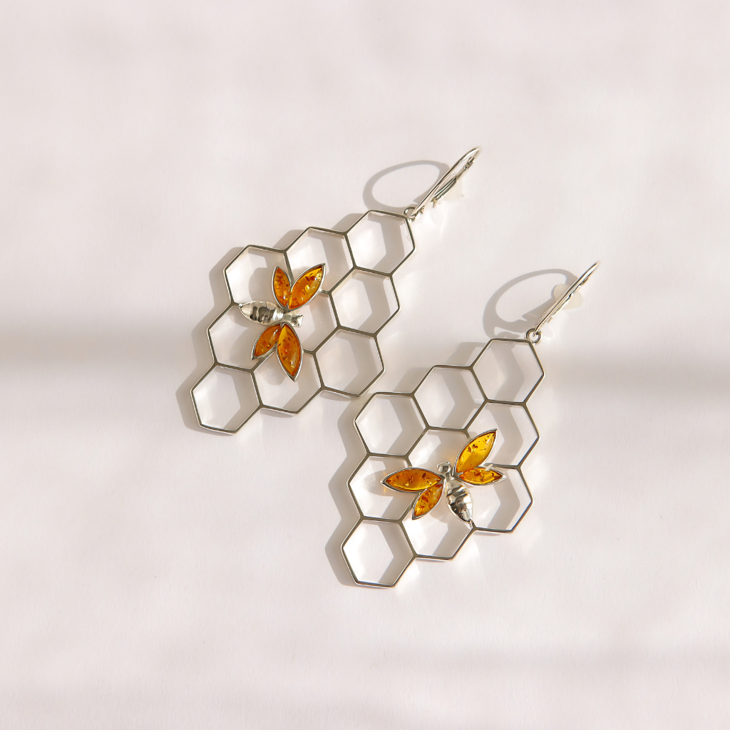 A pair of silver-toned dangle bee earrings featuring a honeycomb pattern with small amber-orange bee charms, displayed on a clean white background.