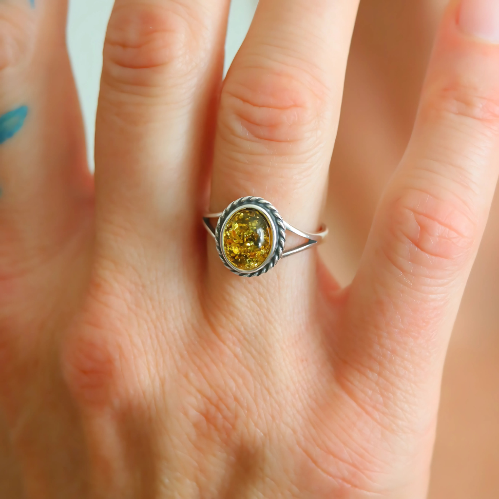 oval cut Ring with a yellow gemstone on a finger against a neutral background