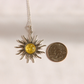 A silver lemon Baltic amber sun pendant necklace with a yellow gemstone center, shown next to a US quarter coin for scale on a plain light background.