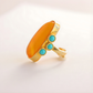 Gold amber ring with orange stone and turquoise beads on a light background