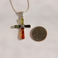 A silver amber cross pendant necklace with a green , lemon, cognac, and orange-red bottom section, displayed next to a US quarter coin to show its size on a plain white background.