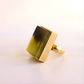 Gold amber ring with a rectangular green stone on a light background