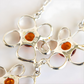 Silver amber flower necklace with circular links and amber-colored stones on a white background