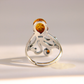 A sterling silver amber octopus ring with a teardrop-shaped amber stone and a smaller accent stone, shown on a light gray background with a soft shadow.