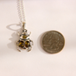 A silver beetle amber pendant necklace with amber-colored gemstones, shown next to a US quarter coin for scale on a plain light background.