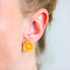 Close-up of an ear wearing a yellow flower earrings with a blurred background