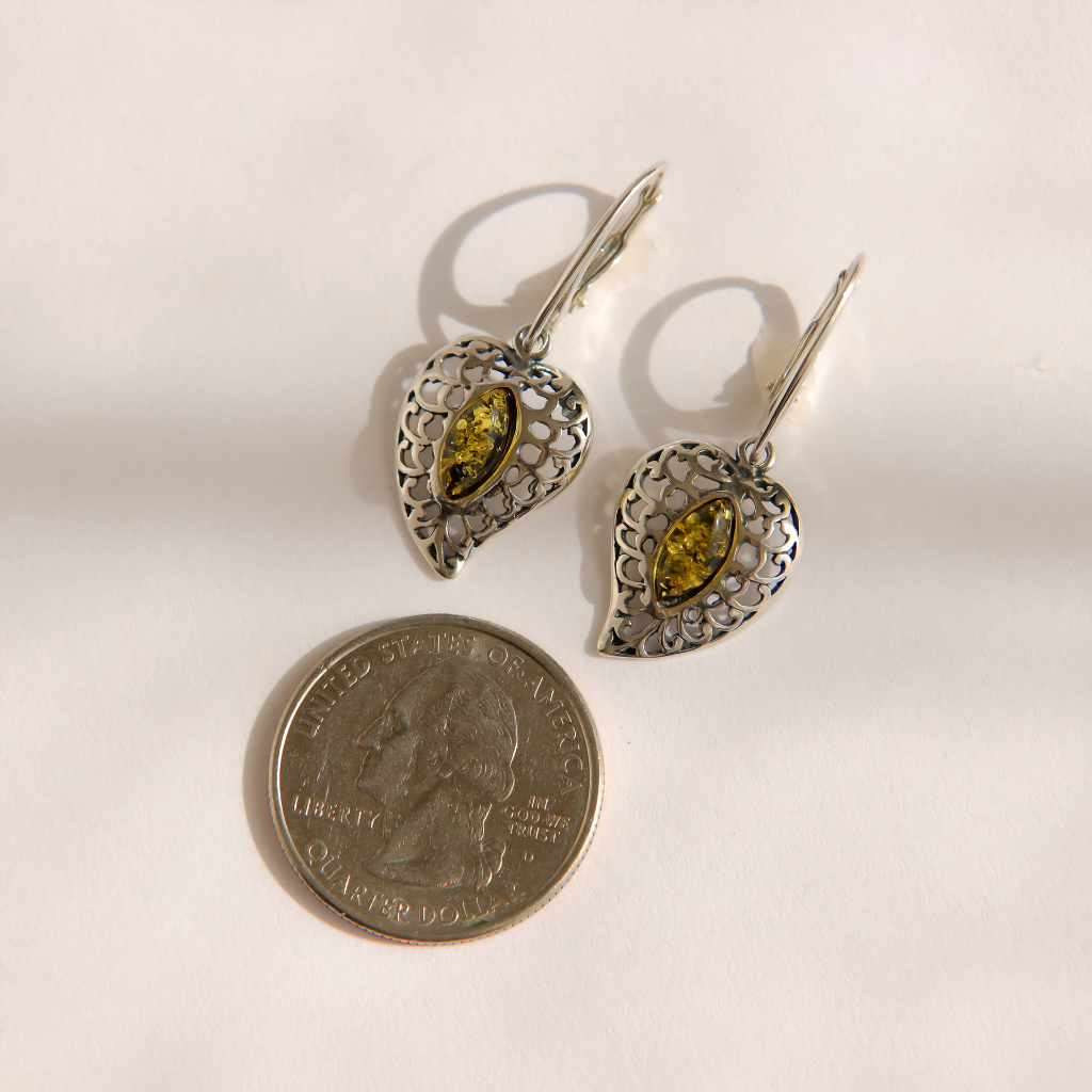 A pair of silver filigree green amber drop earrings with marquise green gemstones, shown next to a US quarter coin for scale on a plain white background.