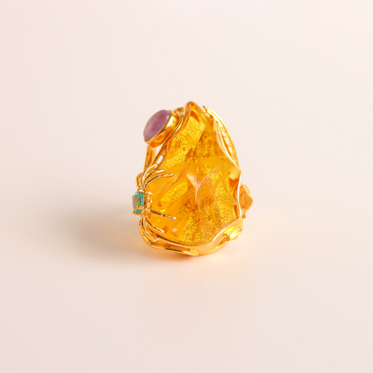 Gold cocktail ring with a central gemstone on a light beige background