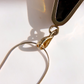 Close-up of a gold-toned green amber pendant clasp and chain on a white surface with a hard shadow cast by bright directional light.