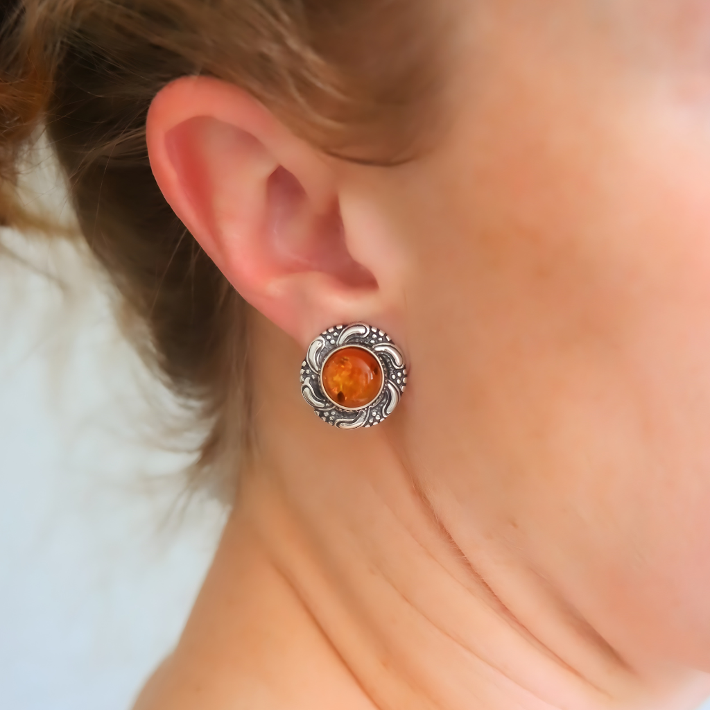 Close-up of an ear wearing silver clip on earrings with a amber stone.
