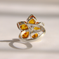 A silver amber flower ring featuring five amber-colored petal-shaped inlays with visible natural inclusions, set on a white background with a soft shadow.