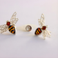 Pair of bee-shaped amber earrings with gold and amber colors on a light gray background
