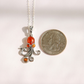 A silver amber octopus pendant necklace with three amber-orange gemstones, shown next to a US quarter coin for scale on a white background.