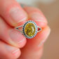 Close-up of a hand holding a silver oval cut ring with a yellow gemstone.