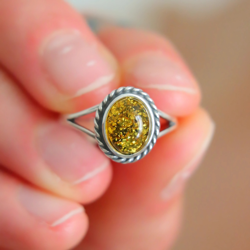 Close-up of a hand holding a silver oval cut ring with a yellow gemstone.