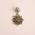 Decorative green amber floral pendant with starburst design and colored stones on a beige background