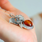 Silver dragon pendant with amber stone held in a hand against a blurred background