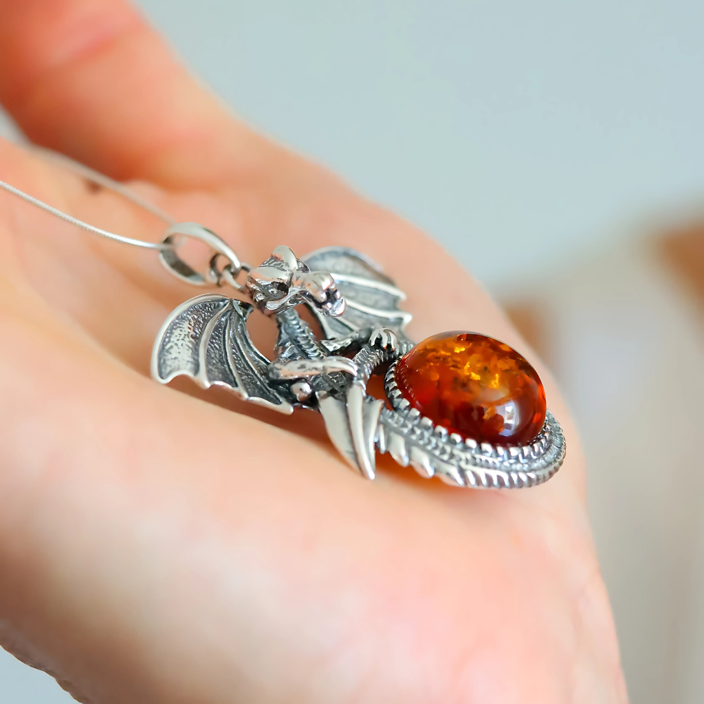 Silver dragon pendant with amber stone held in a hand against a blurred background