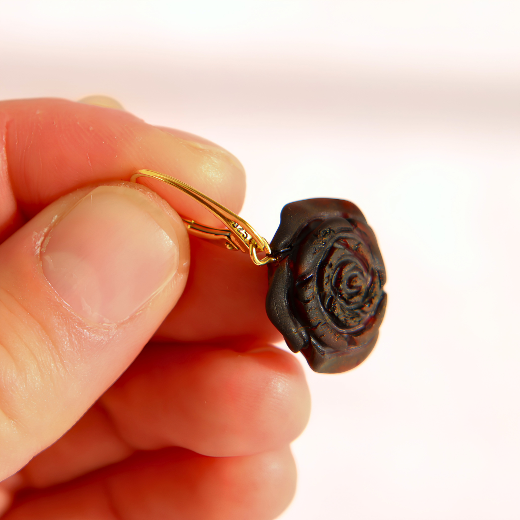 A close-up of a hand holding a small amber rose earrings with a gold-tone leverback closure. T