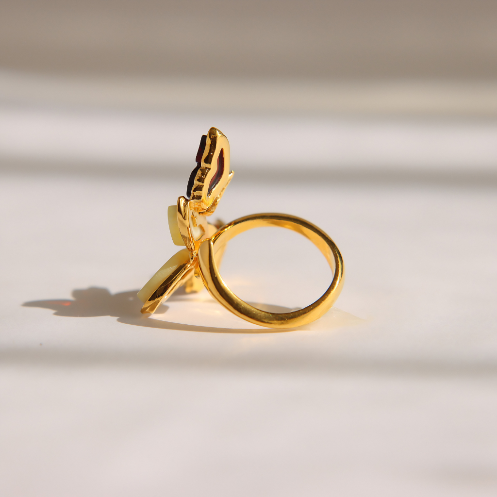 A gold amber butterfly ring featuring a sculpted butterfly design on the band, photographed on a clean white surface with soft shadows.