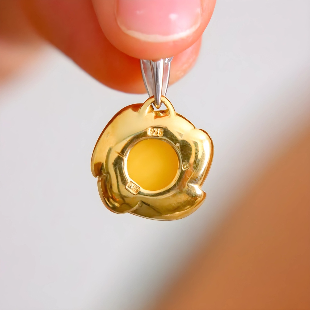Gold pendant with a yellow center held by a hand against a blurred background