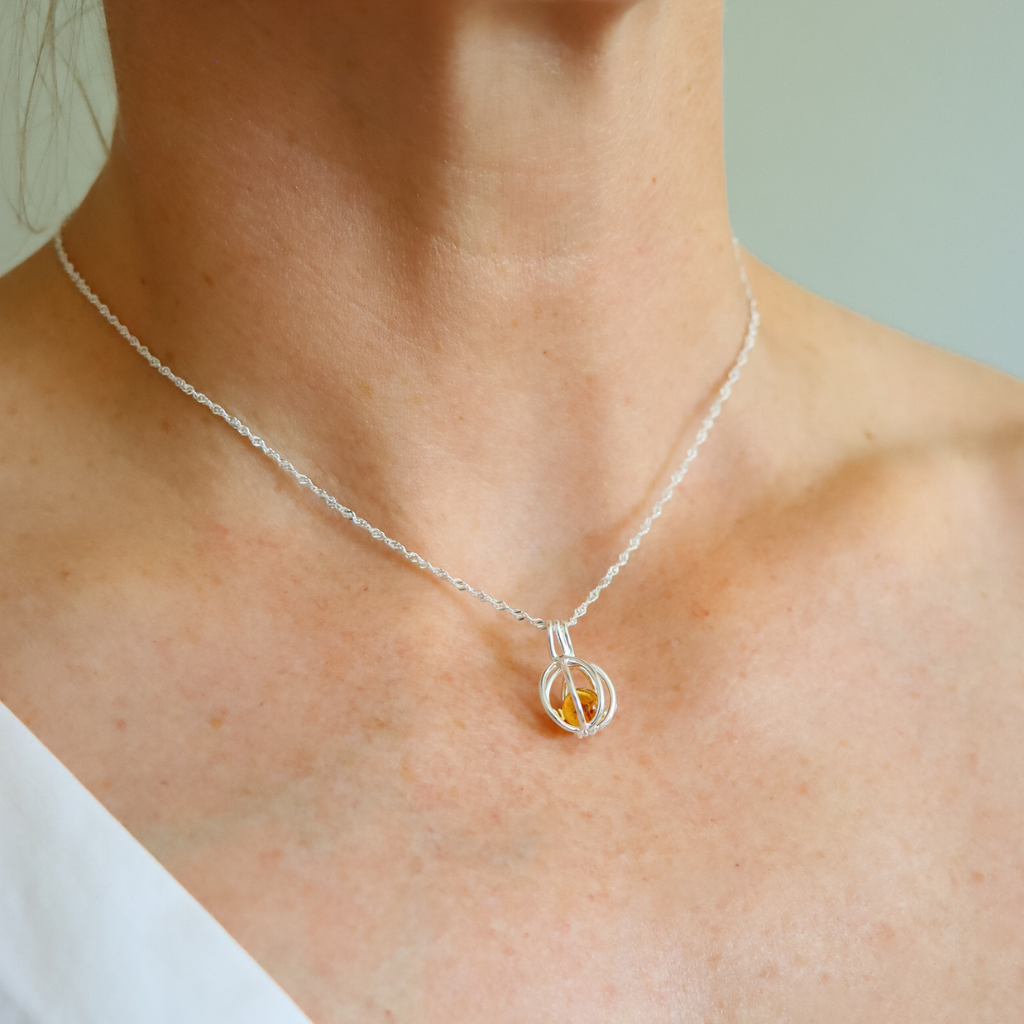 Silver necklace with a small round cage pendant on a person's neck against a neutral background