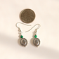 A pair of silver-toned western malachite dangle earrings with green beads and oval filigree charms, shown next to a US quarter coin for scale on a plain light background.