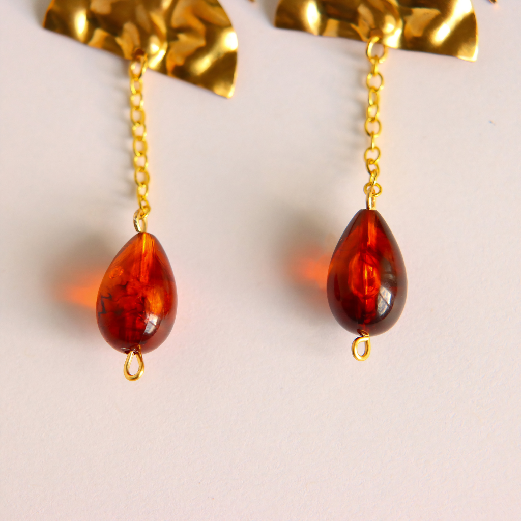 Teardrop-shaped vintage Lucite amber  drop earrings with gold-tone chains displayed against a light off-white background.
