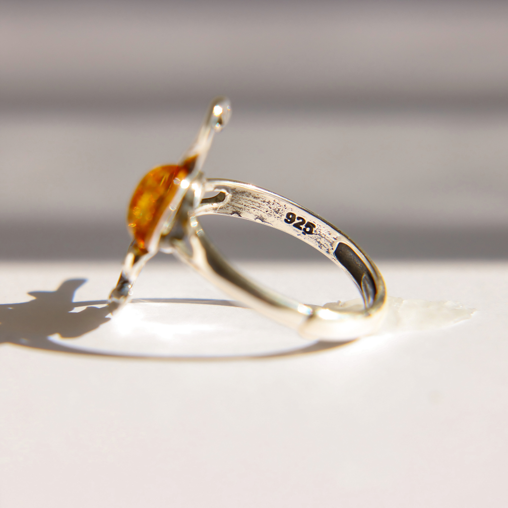 A sterling silver amber dragon ring with a cabachon cut amber gemstone, shown from an angle to display the '925' silver stamp on the band, resting on a white surface with a soft shadow.