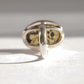 A silver amber cameo ring with an oval face featuring a black amber stone and carved fairy design, photographed in bright sunlight on a light surface.