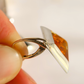 A close-up shot of a hand holding a silver amber earring with a large, polished, asymmetrical amber-colored stone.