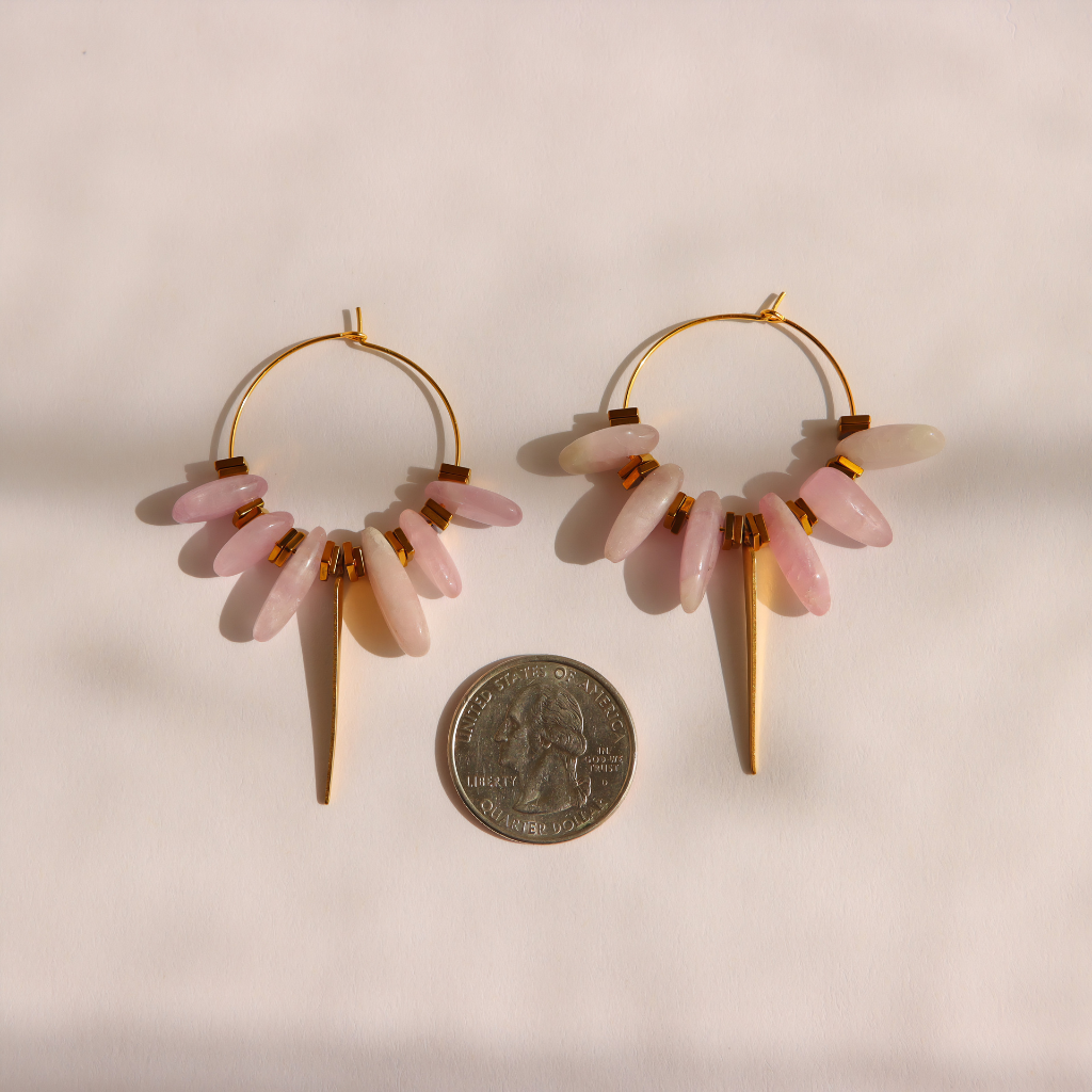 Gold kunzite dagger hoop earrings with multiple pale pink stone drops, shown on a light beige background with a coin for scale.