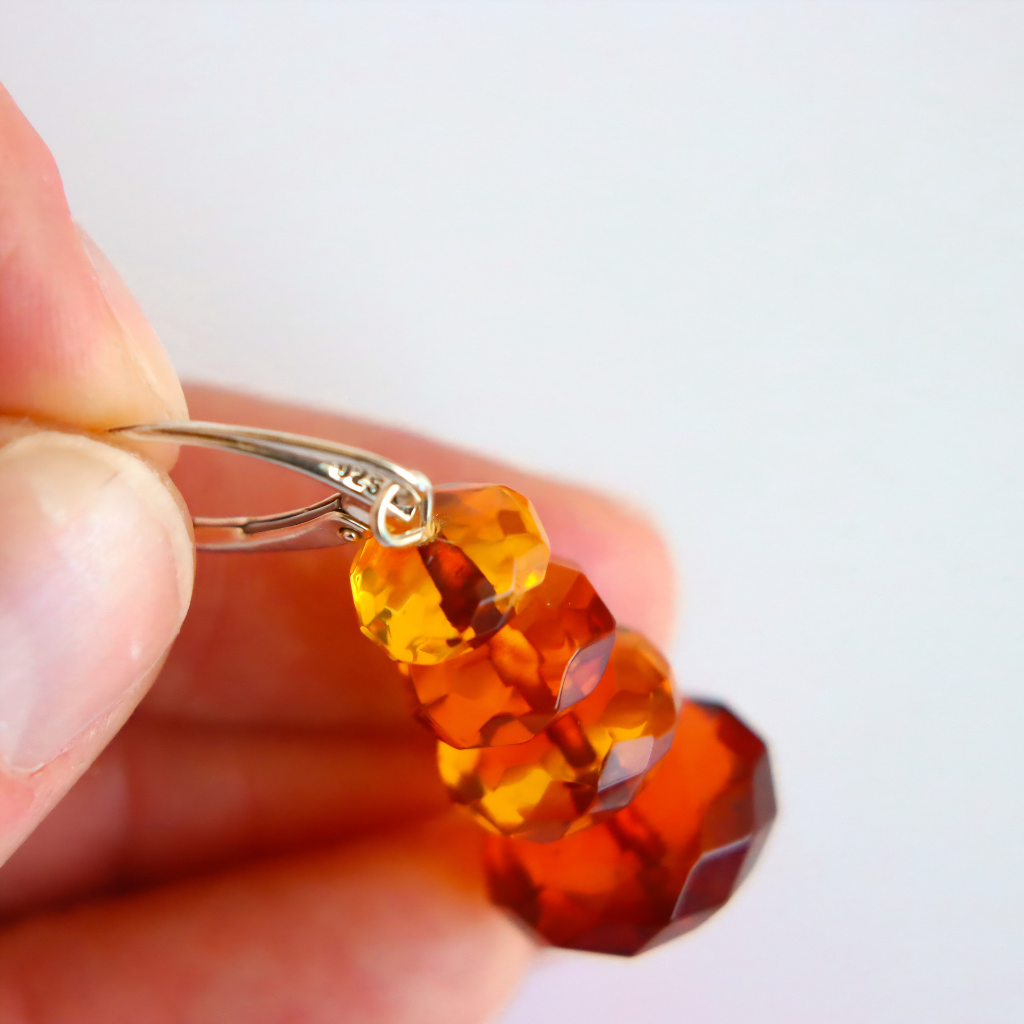 orange and red amber drop earrings being held up close for 925 stamp