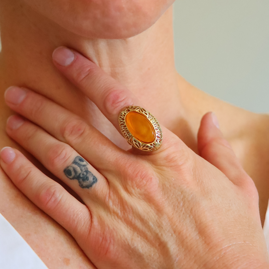 Close-up of a hand with a gold amber ring featuring a yellow stone, with a tattoo on the wrist.