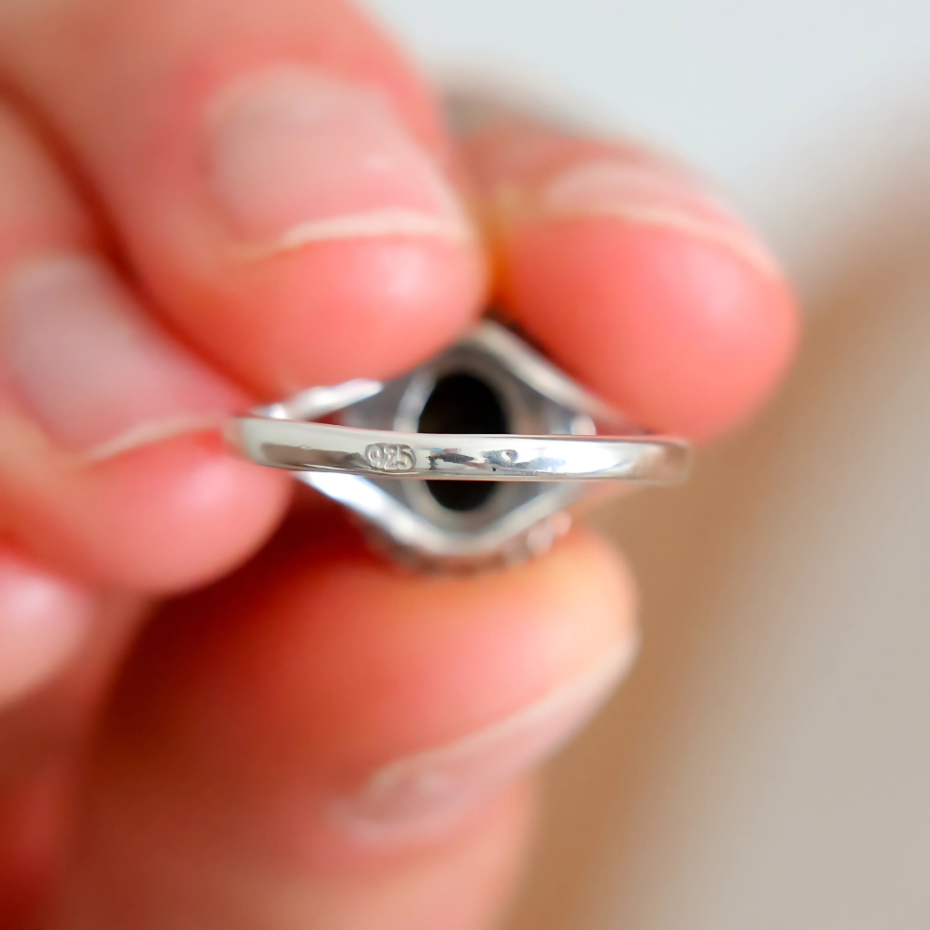 Silver oval cut ring held between fingers showing 925 stamp with a blurred background