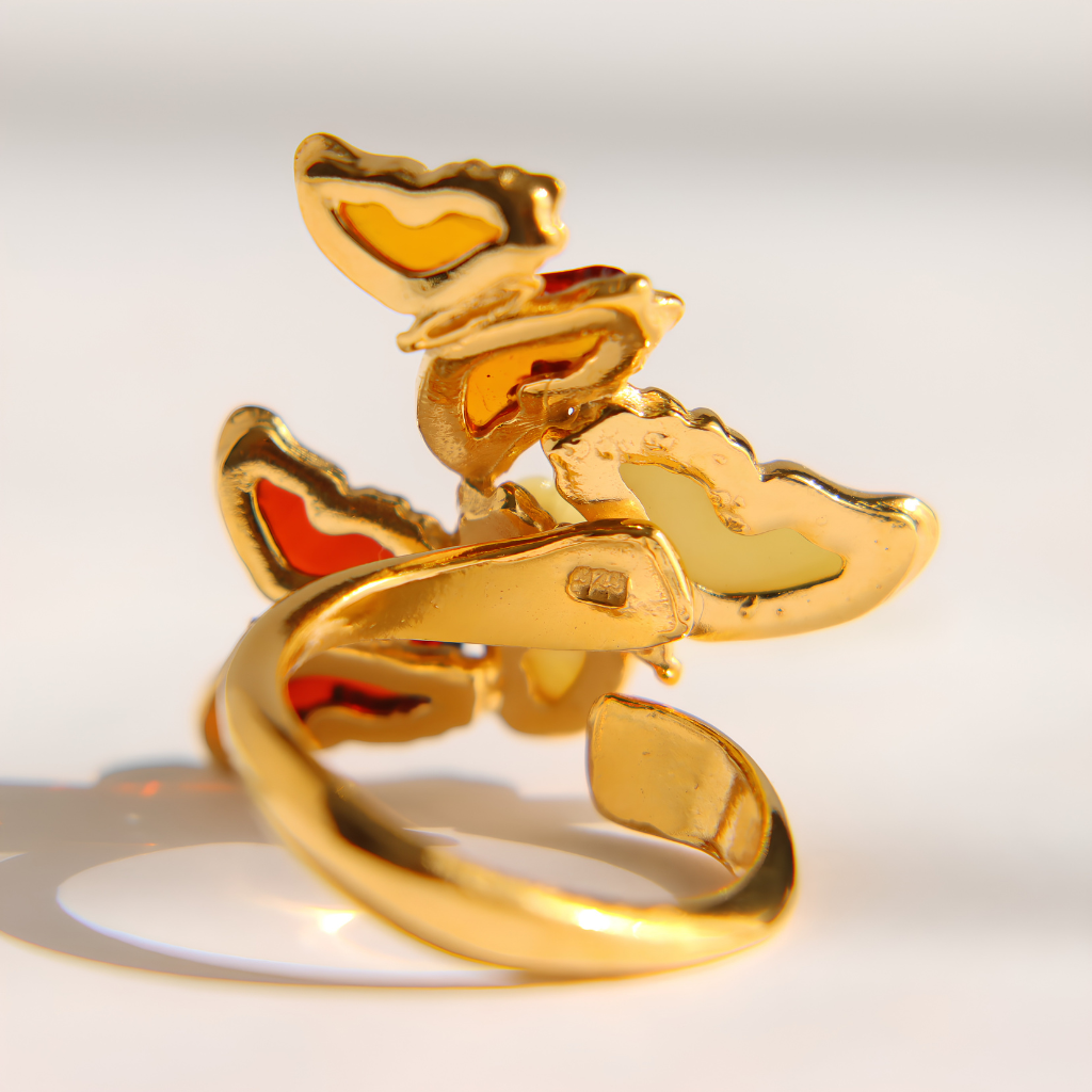 A gold-plated amber butterfly ring with colorful enamel wings in yellow, orange, and light green, set against a bright white background.