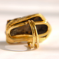 A gold amber statement ring with a textured, organic-shaped setting and two smooth, parallel inner bands, photographed on a white surface with soft shadows.