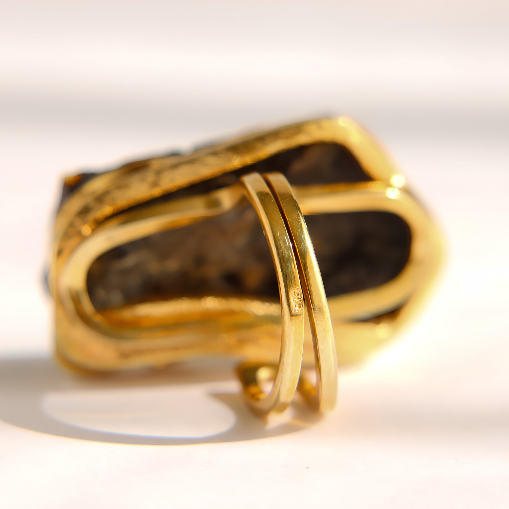 A gold amber statement ring with a textured, organic-shaped setting and two smooth, parallel inner bands, photographed on a white surface with soft shadows.