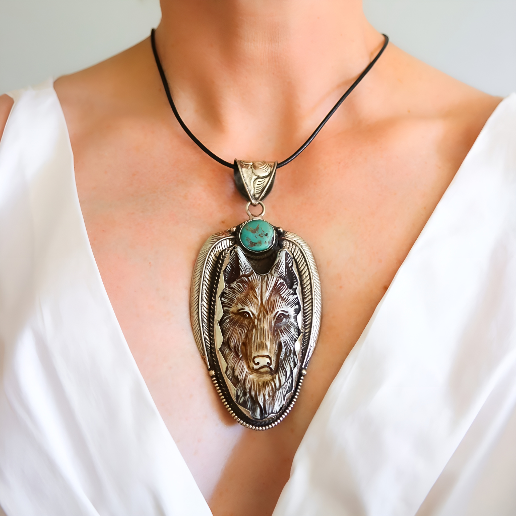 wolf Necklace with a wolf pendant and turquoise stone worn by a person in a white outfit.