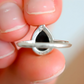 Close-up of a silver amber ring held between fingers with a blurred background