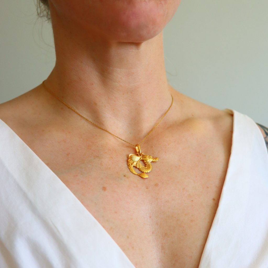 Gold necklace with a dragon pendant worn by a person in a white top.