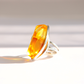 A silver amber statement ring featuring a large, faceted marquise-cut amber gemstone, photographed on a clean white surface with soft shadows.
