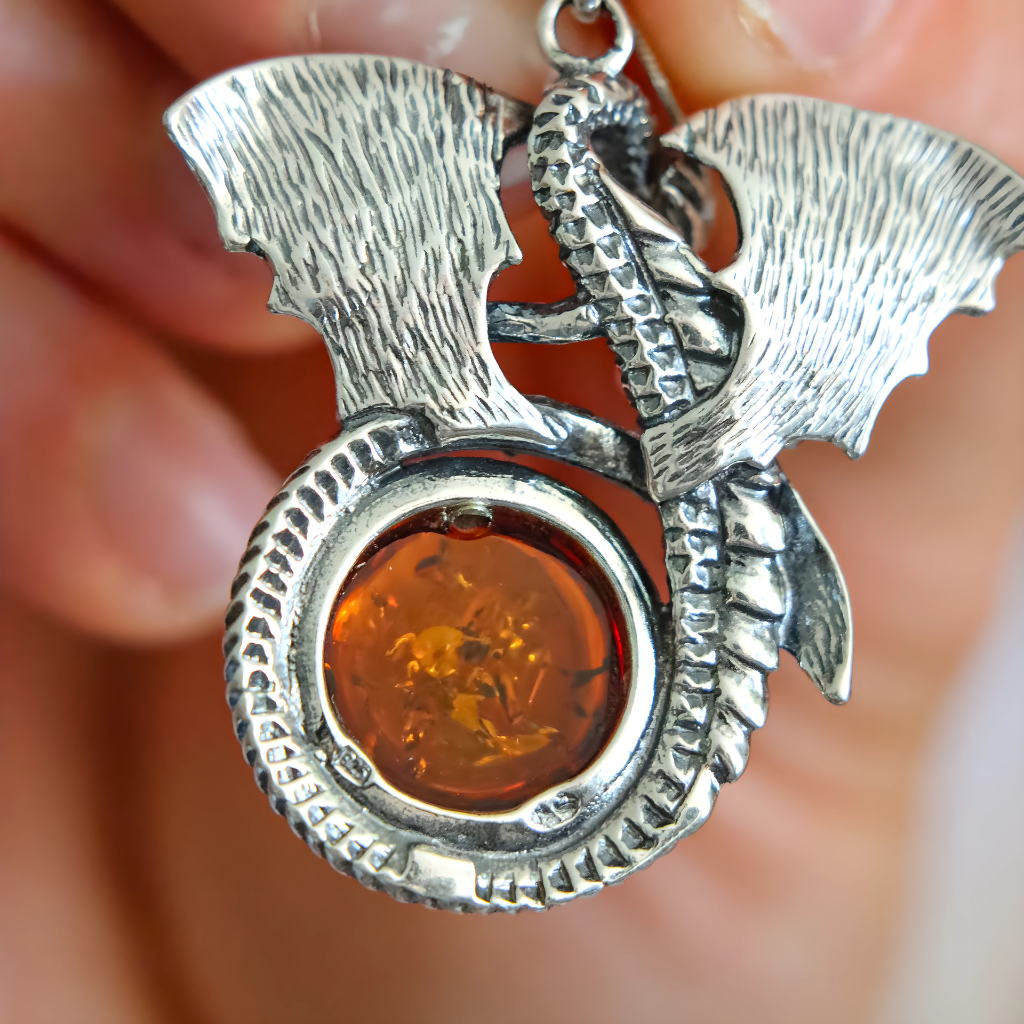 Silver dragon pendant with amber stone held between fingers against a blurred background