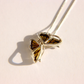 A silver amber butterfly pendant necklace with amber-colored wings, resting on a light cream surface with a soft shadow.