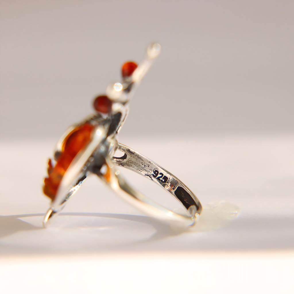 A sterling silver amber snail ring with a large amber-orange marquise-cut gemstone and smaller round amber accents, shown on a light gray background with a '925' hallmark visible on the band.