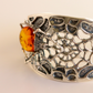 Silver amber bracelet with intricate design and a central cognac amber stone on a beige background