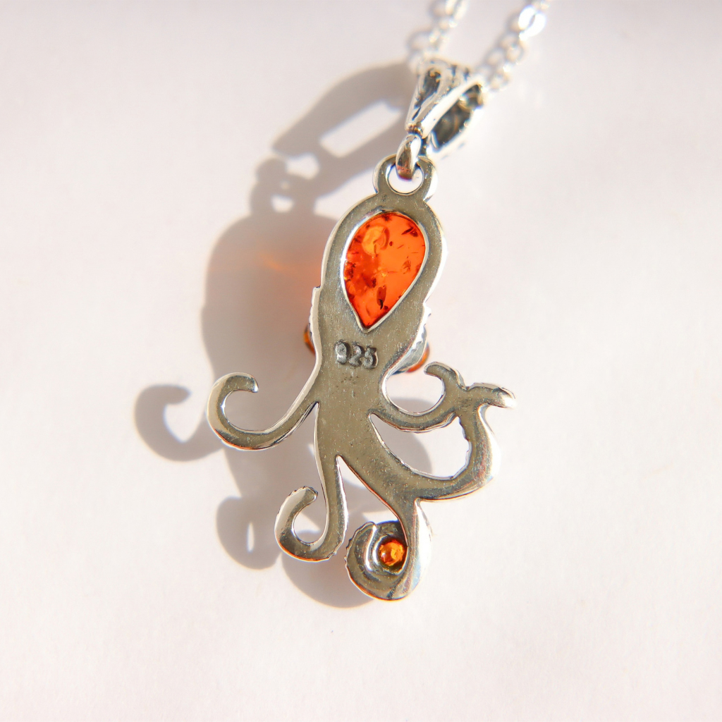 A amber sterling silver octopus pendant necklace featuring a teardrop-shaped orange gemstone on the main body and a small orange stone on one of the tentacles, shown on a white background with a soft shadow.
